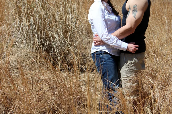 Pareja joven de pie juntos y abrazándose unos a otros en el campo de hierba bajo cielos soleados — Foto de Stock