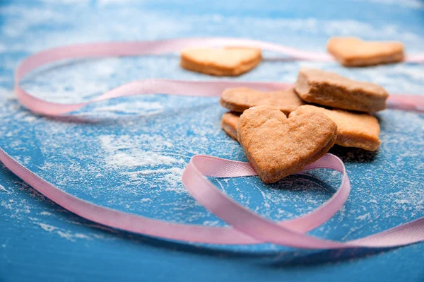 Galletas-corazones sobre un fondo azul con una cinta rosa — Foto de Stock