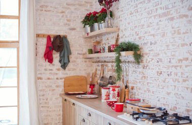 Tuğladan duvarları, kırmızı Noel süslemeleri ve ışıkları olan aydınlık mutfak.