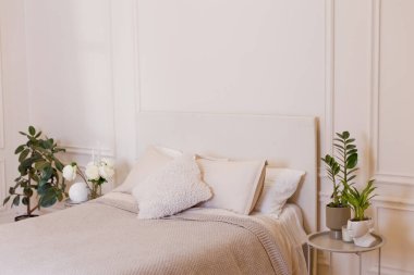 Beyaz duvarları, büyük yatağı, yastıkları ve çiçekleri olan açık renkli bir yatak odası. Boşluğu kopyala, metin için yer