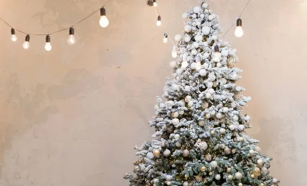 Christmas tree with vintage golden decorations and lights garland near light wall