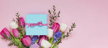 Güzel bir buket ve pembe arka planda kurdeleli mavi hediye kutusu. Fotokopi alanı ile tatil konsepti, metin için yer. 8 Mart, anneler günü teması