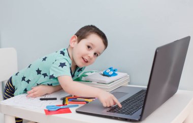 Çevrimiçi eğitim konsepti. Kulaklık takan küçük beyaz bir çocuk internette bilgisayar ve evde eğitim kavramlarıyla ilgili video çalışmaları yapıyor. Anaokulu çevrimiçi çalışması