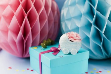 Mavi arka planda pembe ve mavi süslemeli cinsiyet belirleme partisi. Erkek ya da kız partisi. Pembe çiçekli mavi bebek arabası vazosu, kurdeleli hediye kutusu ve büyük kağıt balonlar.