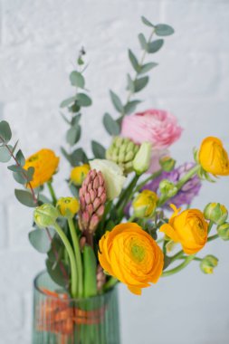 Turuncu ve pembe ranunculus çiçekli güzel bir buket, okaliptüs ve beyaz arkaplanda yeşil bir vazoda sümbül.