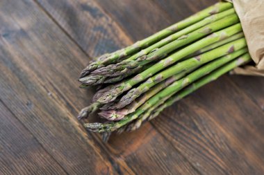 Taze yeşil kuşkonmaz, ahşap arka planda kahverengi kağıt.