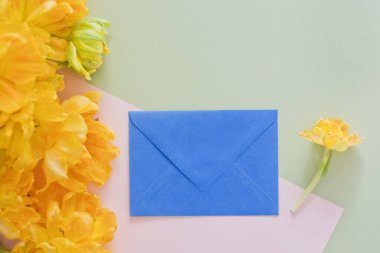 Çiçeklerin yanında bir hediye. Mavi zarf, hediye kartı ya da sarı lale buketinin yanındaki mektup. Bahar tatili konsepti, hediye fikri. Boşluğu kopyala, metin için yer