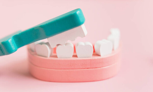 Dental background with wooden toy jaw, teeth and toothbrush on a pink background. Dentistry, dentist clinic concept.