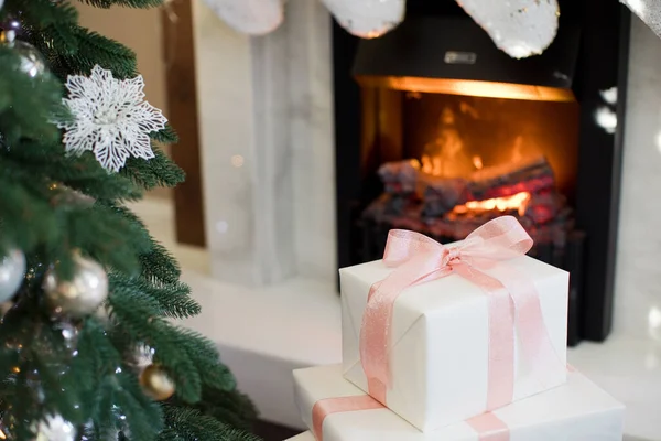 靠近壁炉和圣诞树的装有粉色缎带的圣诞礼品盒 — 图库照片