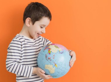 Caucasian boy holds globe on an orange background with copy space
