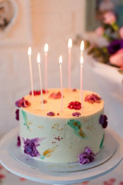 Doğum günü pastası ve beyaz pasta standında yanan mumlar güzel bir buket çiçeğin yanında. Mutlu yıllar hediye konsepti