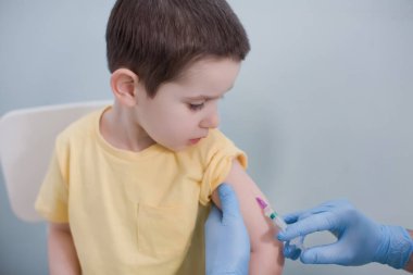 Aşı konsepti. Mavi eldivenli doktor klinikte sarı tişörtlü çocuğu aşılıyor.