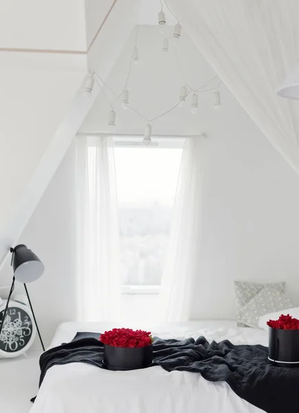 Light rooftop duplex bedroom with window. Beautiful bedroom with black blanket, box with red roses, big window, lamp and clock. Stylish minimal interior
