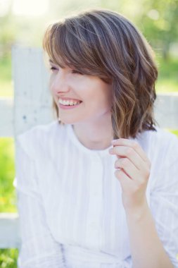 Beyaz elbiseli güzel beyaz kadın bahar çiçekleri bahçesinde beyaz ahşap çitlerin yanında yürüyor.