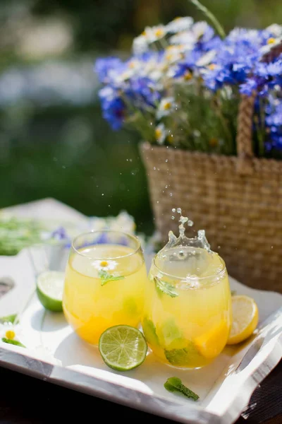 ミント ライム レモン オレンジのレモネードグラスは 野花のあるわら袋の近くの白い木製のトレイにあります 夏のドリンクコンセプト — ストック写真