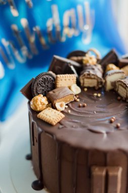 Chocolate cake with various sweets and blue star shaped balloon with happy birthday sign