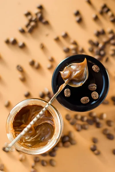 Jar with caramel sauce, metal vintage spoon and coffee beans on a brown background. Coffee caramel sauce taste