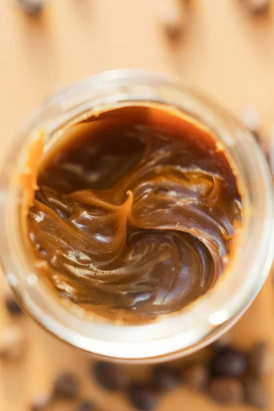 Jar with caramel sauce and coffee beans on a brown background. Coffee caramel sauce taste