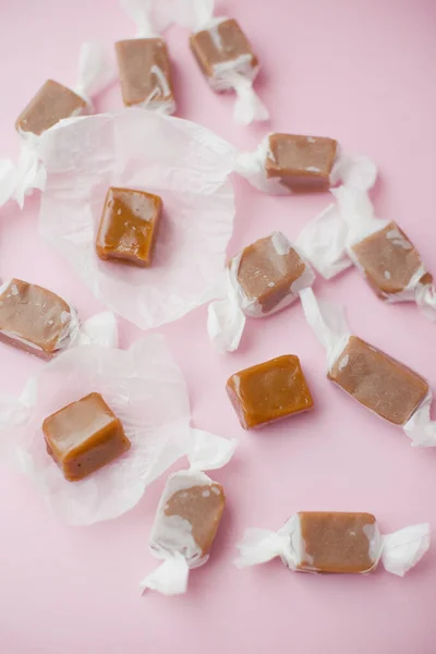 Caramel candy fudge in paper wrapping on a pink background
