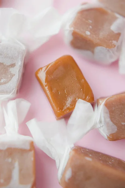 Caramel candy fudge in paper wrapping on a pink background