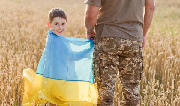 Military man and child with Ukraine flag in wheat field. Ukraine independence day concept. Stop war in Ukraine. Save Ukraine