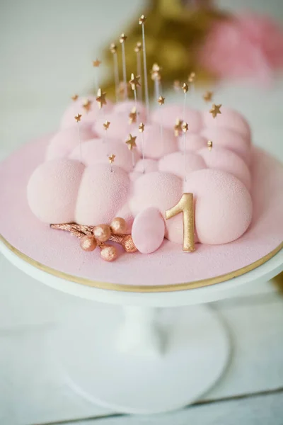 Pink cake with golden star decorations on a white cake stand. First birthday party concept
