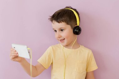 Caucasian boy in headphones holding smartphone on a pink background with copy space