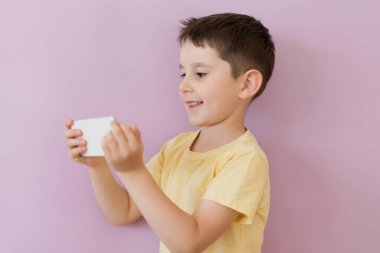 Caucasian boy in yellow t-shirt holding smartphone on a pink background with copy space