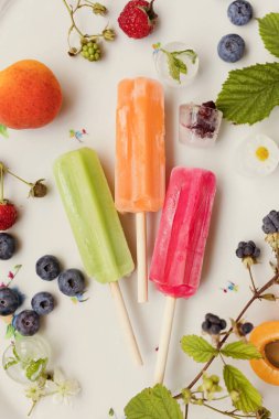 Bright colorful popsicles on a white tray with berries and ice cubes on a light violet background. Tasty ice pops close up