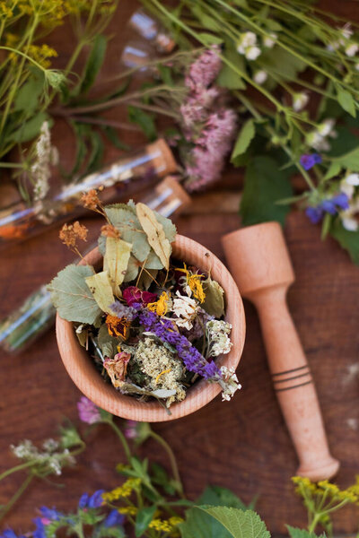 Homeopathy and herbal medicine concept. Wooden mortar and pestle with dry herbs, wildflowers, chalkboard and glass bottles on a wooden background