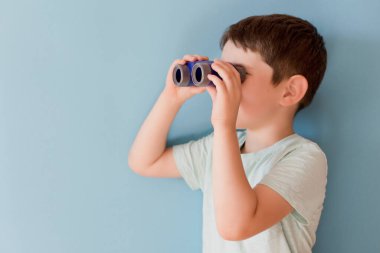 Caucasian boy with toy binoculars on a blue background with copy space. Travel funny concept