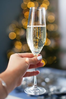 Woman holds glass of champagne on a Christmas tree lights background. New year eve concept
