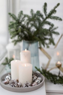 Bouquet of green spruce branches in vase, white burning candles and star decoration at home interior