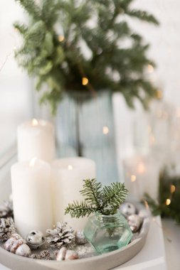 Bouquet of green spruce branches in vase, white burning candles and star decoration at home interior