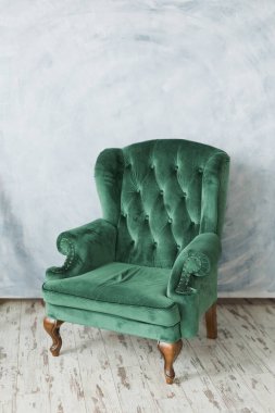 Green emerald velvet armchair near empty white wall with copy space