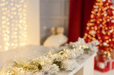 Kırmızı Noel ağacının yanındaki masada beyaz Noel çelengi