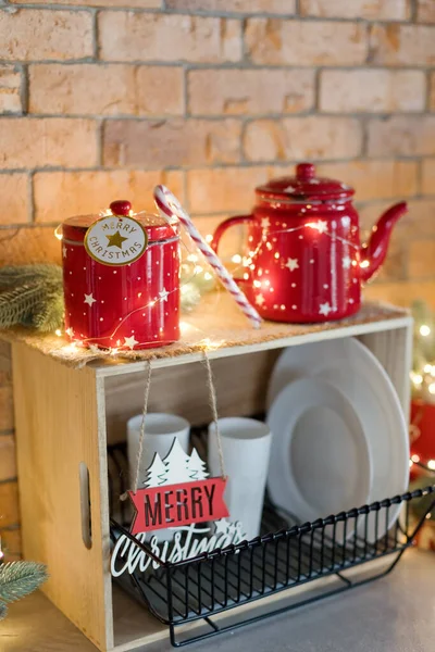 Vintage red metallic kettle, kitchen tableware and Christmas lights decorations near brick wall