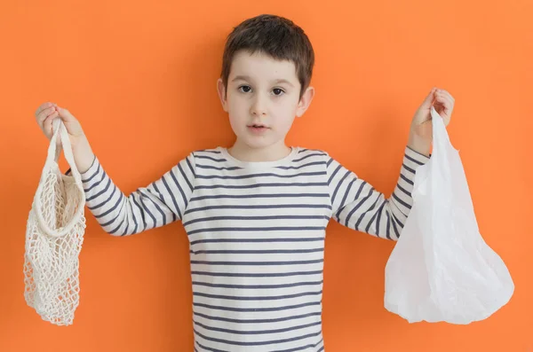 Child with cloth and plastic bag on an orange background with copy space, ecology concept. Choosing plastic or cloth bag, save planet, zero waste