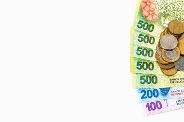 Arjantin pezosu 500, 200 ve 100 'lük banknotlar beyaz bir arka plana yayıldı ve masanın sağ tarafından bir yığın bozuk para görüldü.