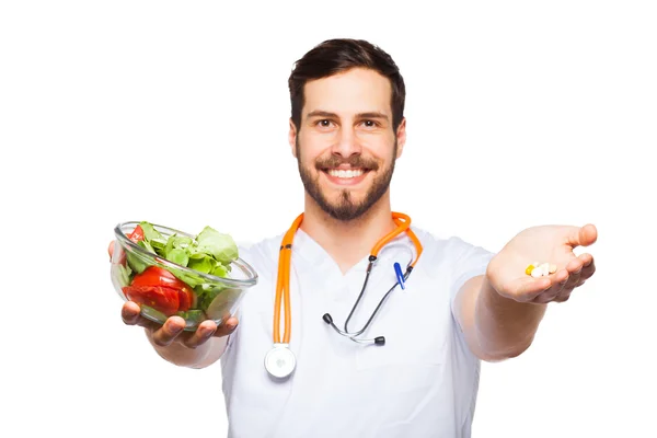 Schöner männlicher Arzt zeigt Salat und Pillen — Stockfoto