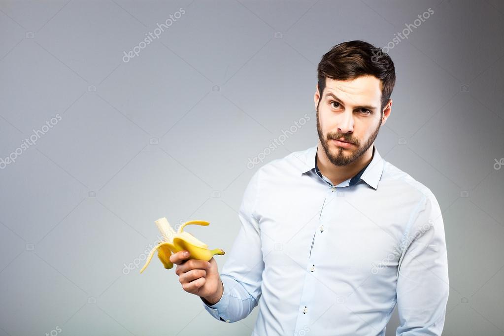 Portrait of a smart serious young man eating banana