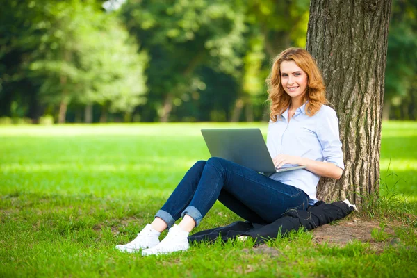 Krásná žena, sedí v parku s notebookem — Stock fotografie
