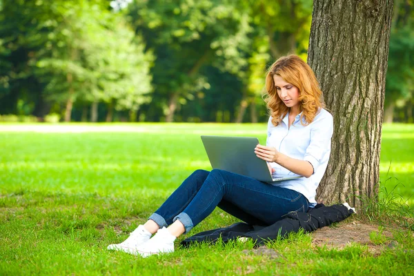 Femeie frumoasă care stă în parc cu laptop — Fotografie, imagine de stoc