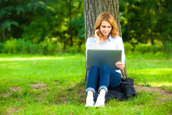 Vakker kvinne som sitter i parken med laptop – stockfoto