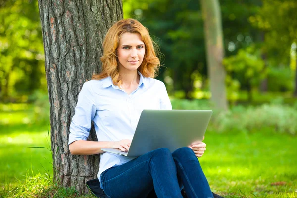 Schöne Frau sitzt mit Laptop im Park — Stockfoto