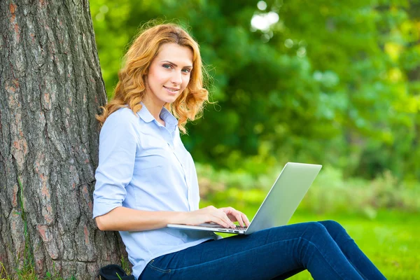 Schöne Frau sitzt mit Laptop im Park — Stockfoto