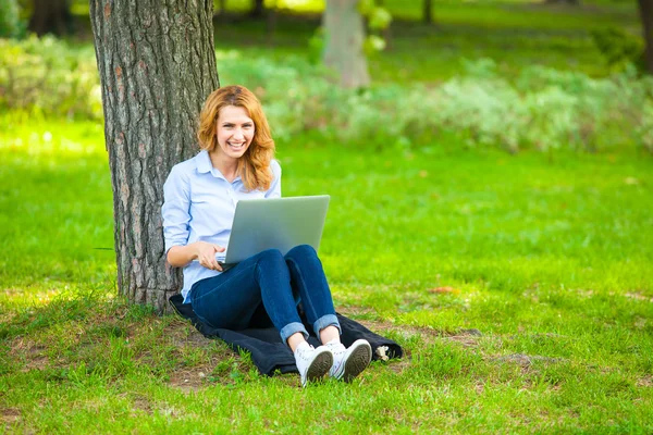 Schöne Frau sitzt mit Laptop im Park — Stockfoto