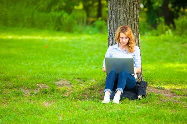 Красивая женщина сидит в парке с ноутбуком — стоковое фото