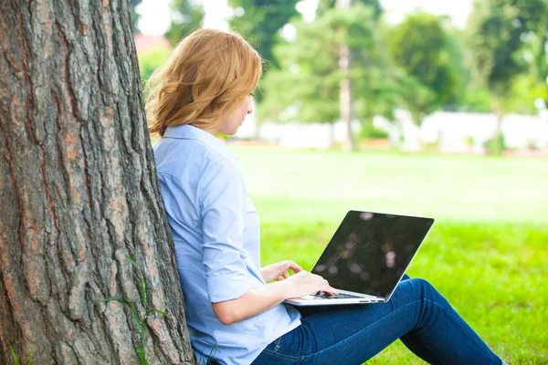 Schöne Frau sitzt mit Laptop im Park — Stockfoto