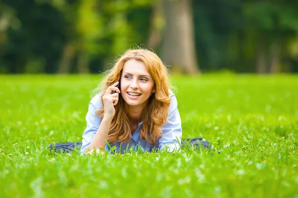 Blondýnka ve svém projevu na mobil v zelené trávě — Stock fotografie